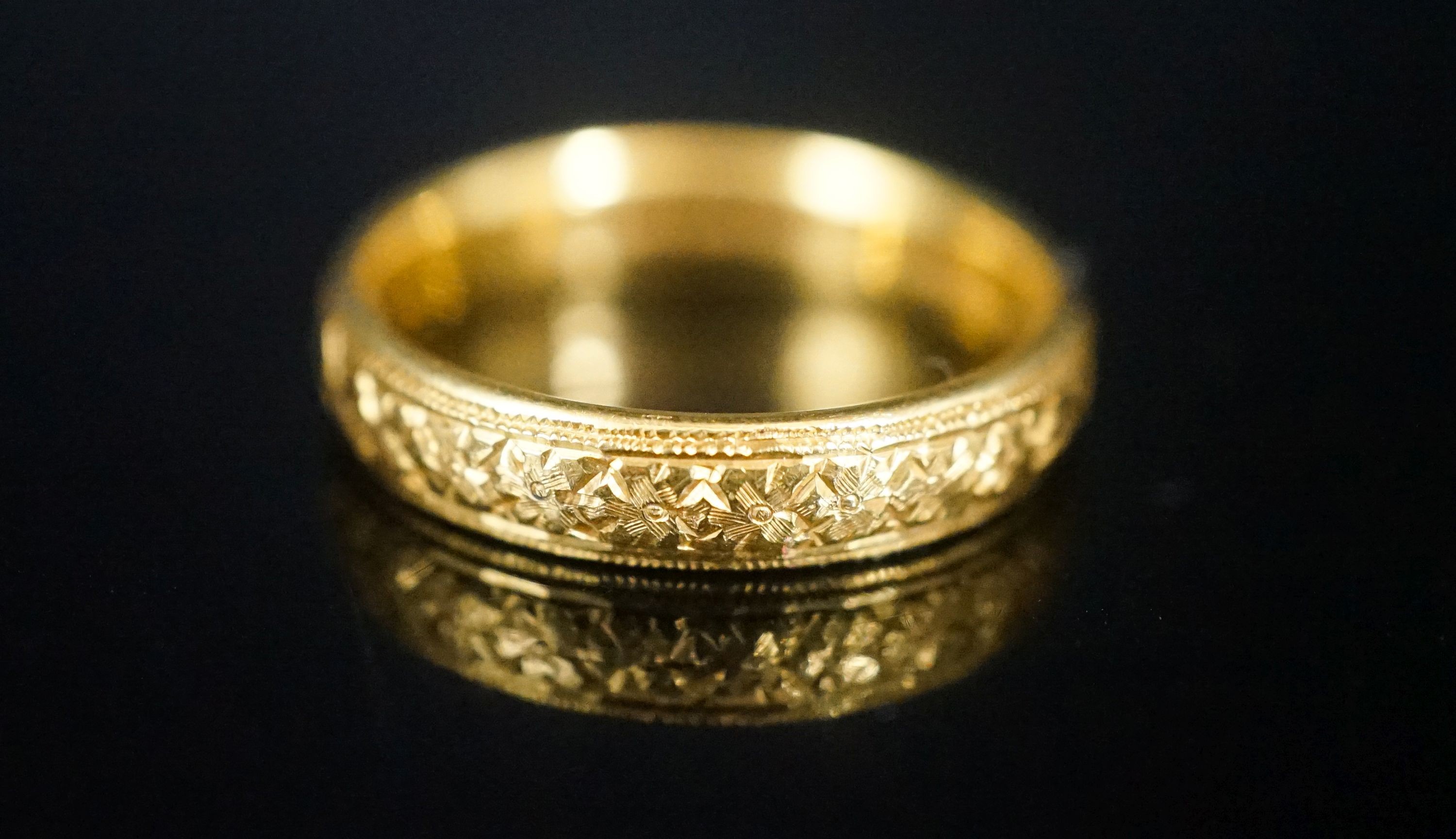A George V bright cut engraved 22ct gold wedding band, decorate with flower heads, London, 1918, size V, 8 grams.